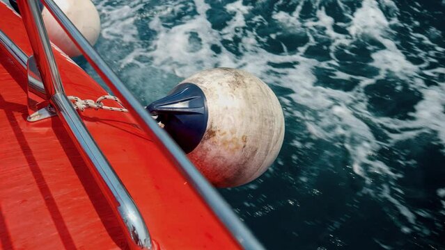 Closeup of fenders and buoys hanging on the side of red rescue boat sailing through cold northern sea.