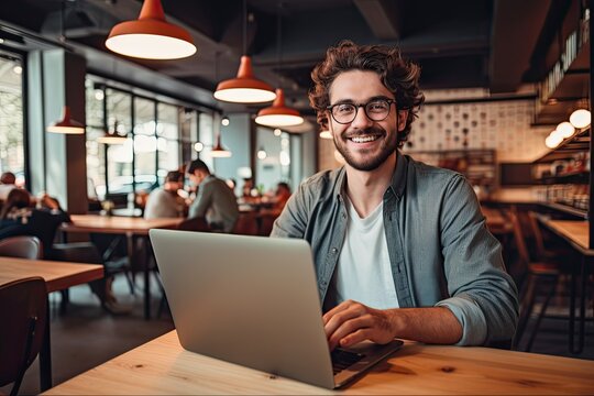 Portrait of Skilled Hipster Guy Freelancing in Cafe Interior. Male IT Developer Typing on Modern Laptop with Smiling Expression