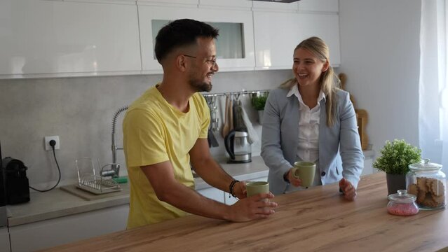 Young man made first coffee for his girlfriend in formal wear who goes to work and they drink it together in the morning in the kitchen while discussing what they will do when she comes home from work