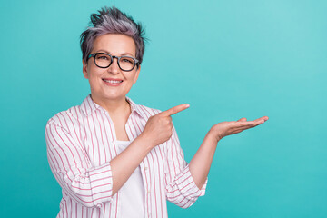 Portrait of charming senior business woman point finger at open palm offer novelty product sale isolated teal color background