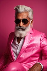 Glamorous portrait of an age old Indian man with beard wearing glasses dressed in pink clothes on pink background.