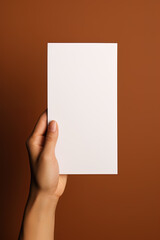 A human hand holding a blank sheet of white paper or card isolated on brown background