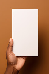 A human hand holding a blank sheet of white paper or card isolated on brown background