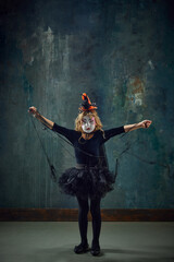 Little girl, child in i witch costume, with creepy makeup standing against dark vintage background. Spooky look. Concept of Halloween, childhood, celebration, party, holiday, creativity, ad