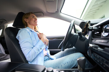 Young happy woman is sitting behind wheel of modern car