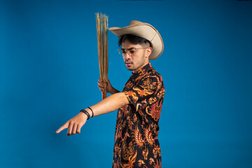 Asian youth wearing a batik shirt holding a broom stick while pointing down