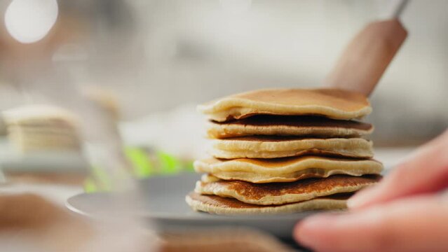 A pile, a pregnant girl with pleasure lays out a bunch of pancakes on a beautiful plate in a cozy atmosphere. Camera in motion young woman stacks ready-made pancakes uses kitchen utensils, baked