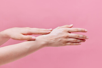 Horizontal image of beautiful, tender young woman hands usinging cream, scrub on her hands on pastel pink background. Anti-aging.