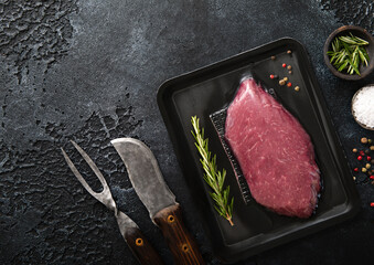 Beef raw fillet steak in vacuum tray with pepper,salt and rosemary on black background with...