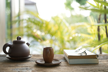 Brown earthenware teapot glasses and tea cup and notebooks on wooden table