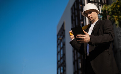 Caucasian male worker at a construction site. Architectural design is holding a laptop at a construction site, checking plans. Successful engineer or architect, cheerful businessman. Builder.