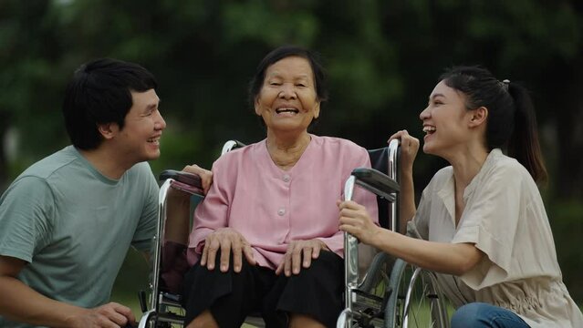 happy grandson and granddaughter talking with senior woman in wheelchair at the park