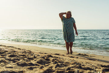 Fototapeta na wymiar beautiful grandmother blonde in a dress walks on the sand on the beach near the sea vacation pension travel