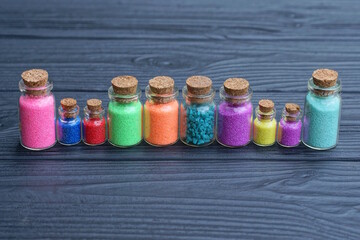 a row of a set of small glass decorative bottles with colored sand stand on a black wooden table