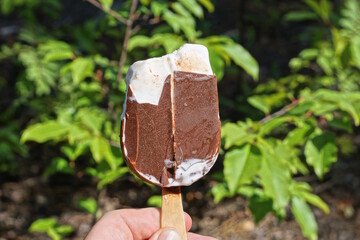 a piece of white ice cream in brown chocolate in his hand on a green background on the street