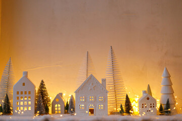 Atmospheric miniature christmas village. Stylish little white houses and trees on snow blanket with glowing lights in evening. Christmas modern winter village, holiday banner. Happy Holidays!