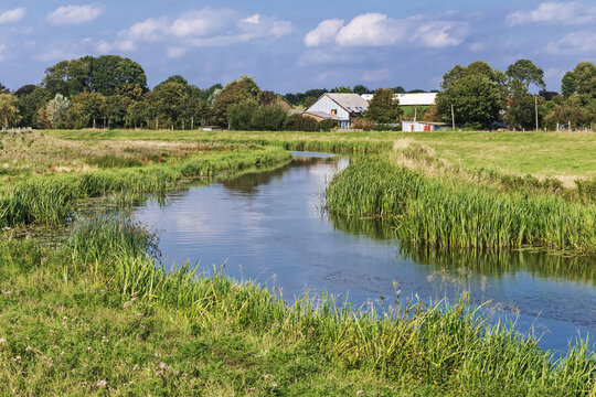 Der Fluss Treene bei Hollingstedt in Schleswig-Holstein, Deutschland im Sommer. Im Hintergund ein Bauernhof.