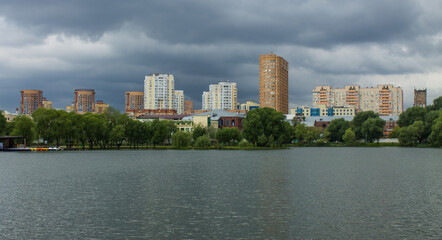 Fototapeta na wymiar beautiful urban landscape - modern residential buildings among green trees on the shore of a pond with reflection and cloudy sky with dramatic clouds. concept - weather and copy space