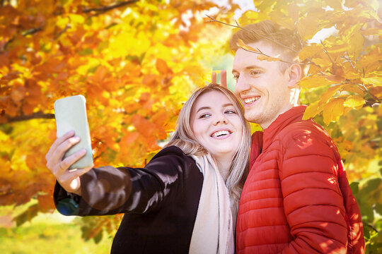 Happy autumn couple taking selfie (photo) in fall park. Smile woman (girl), man (boyfriend) having fun. Yellow leaves. Healthy lifestyle, sale, Black Friday, fall concept..