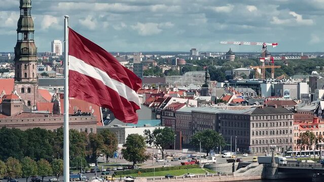 Beautiful Latvian flag flutters in a wind with Riga old town in the background in Latvia. Patriotic video. Riga aerial view.