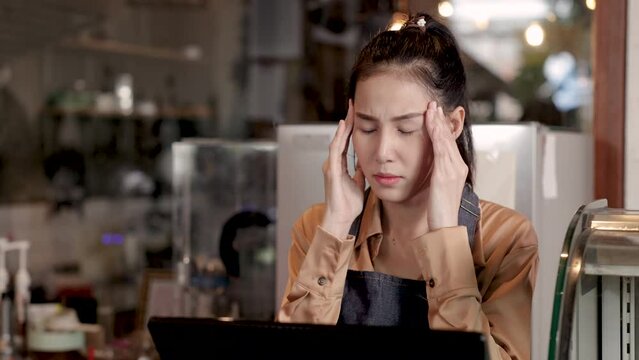 Asian young barista girl get headache and frustrated with over-expenses in cash register machine, senior elderly retirement mother worried with daughter about investment in small business coffee shop