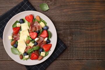 Tasty salad with brie cheese, prosciutto, almonds and berries on wooden table, top view. Space for text