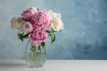 Beautiful peonies in glass vase on white table. Space for text