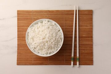 Bowl with delicious rice and chopsticks on white marble table, top view