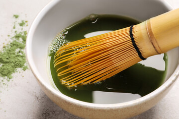 Bowl of fresh matcha tea with bamboo whisk on light table, closeup