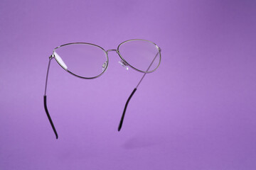 Stylish pair of glasses with metal frame on purple background. Space for text