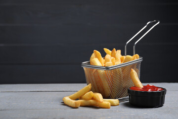 Tasty French fries served with ketchup on grey wooden table. Space for text