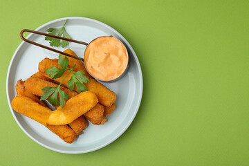 Tasty fried mozzarella sticks served with sauce and parsley on green background, top view. Space for text