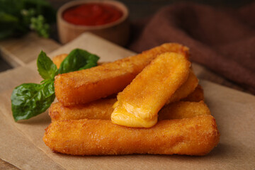 Tasty fried mozzarella sticks and basil on table, closeup