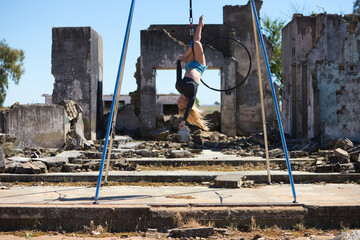 Young and beautiful blonde woman, spectacular exercise on an aerial hoop. She does different artistic and acrobatic poses. The young athlete is among the ruins of a building. Sport concept.