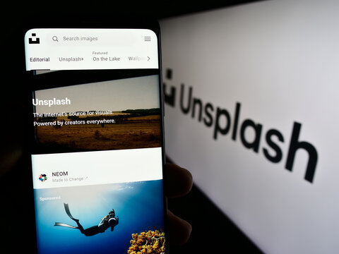 Stuttgart, Germany - 08-18-2023: Person holding smartphone with webpage of stock photography company Unsplash Inc. on screen in front of logo. Focus on center of phone display.