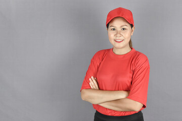 Portrait of a young delivery woman with pleasant smile and crossed arms on grey background with copy space.