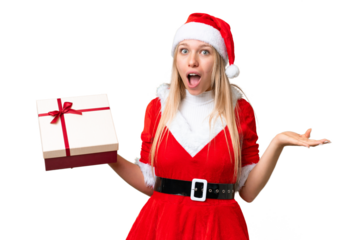 Young blonde woman with christmas hat and holding a gift over isolated chroma key background with shocked facial expression