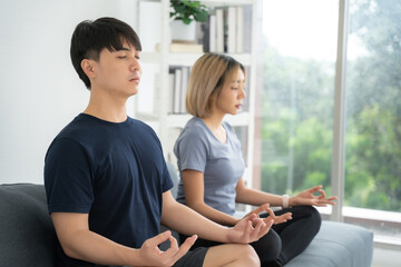 Asian people sitting on sofa and doing yoga together at home. Healthcare and Yoga concept.