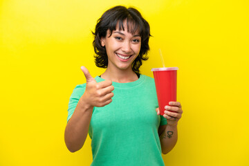 Young Argentinian woman holding a soda isolated on yellow background with thumbs up because something good has happened