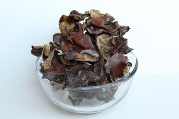 Dried jelly ear, or wood ear fungus, or black mushrooms, or Auricularia auricula judae, in transparent bowl. Isolated on white background