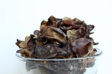 Dried jelly ear, or wood ear fungus, or black mushrooms, or Auricularia auricula judae, in transparent bowl. Isolated on white background