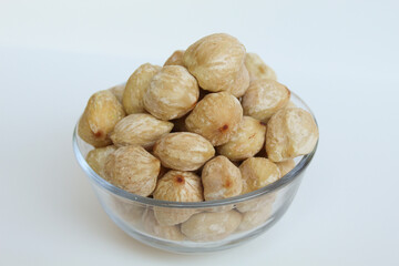 Dried Indonesian Candlenuts, or Kemiri, the seed of Aleurites moluccanus inside a transparant bowl, isolated in white background