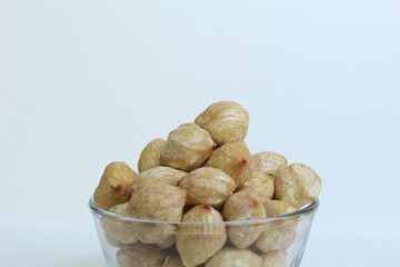 Dried Indonesian Candlenuts, or Kemiri, the seed of Aleurites moluccanus inside a transparant bowl, isolated in white background