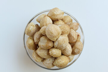 Dried Indonesian Candlenuts, or Kemiri, the seed of Aleurites moluccanus inside a transparant bowl, isolated in white background. Flat lay or top view