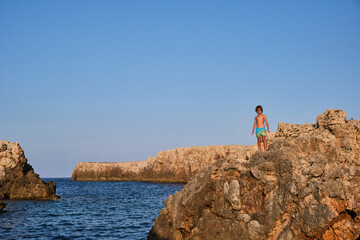 Boy standing on rock near blue sea