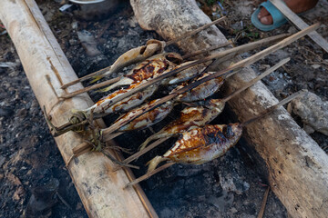 Grilling fresh fish on bamboo skewers with sweet soy sauce (kecap manis) as seasoning on the beach. A simple and traditional way.