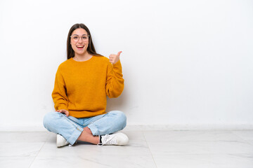 Young girl sitting on the floor isolated on white background pointing to the side to present a product