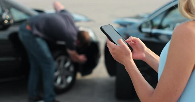 Woman insurance agent inspects damage to a man car and makes notes on a smartphone. Woman inspecting broken car. Insurance concept.