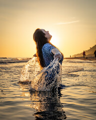 radosna dziewczyna kapiąca się w morzu o wschodzie słońca, chlapiąca wodą - obrazy, fototapety, plakaty