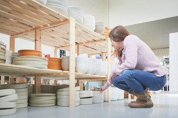 Shopping in a pottery store. Young woman looking for ceramic tableware and utensils in a craft shop.